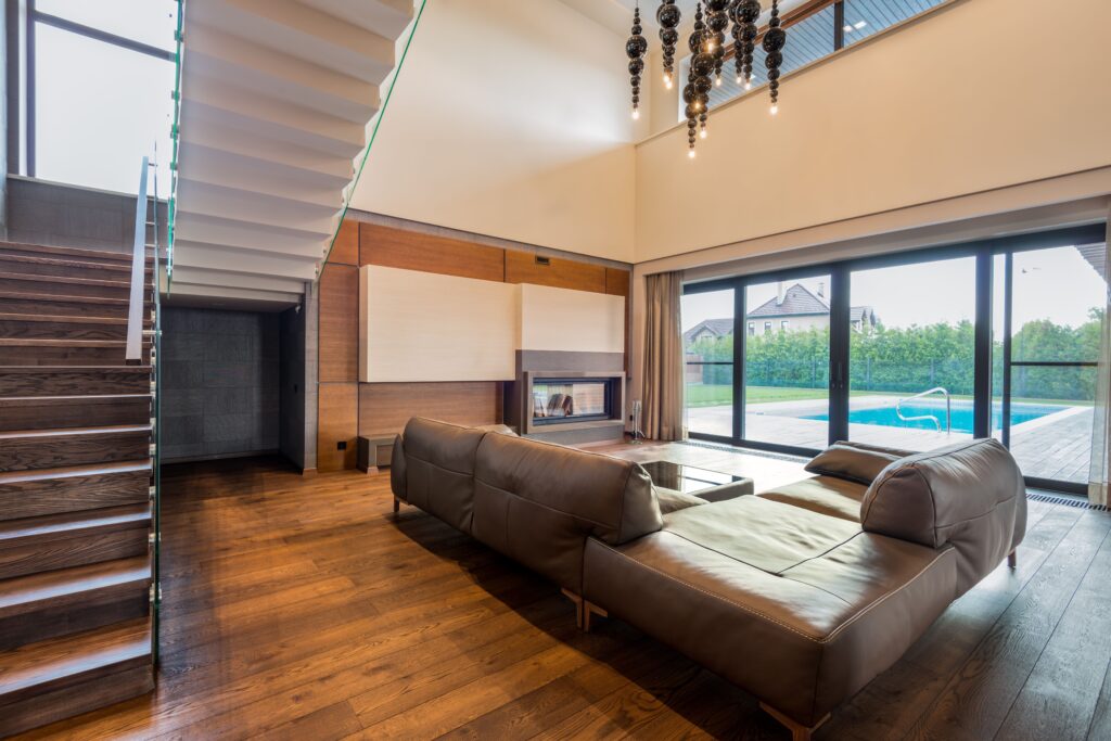 Spacious luxury living room design in Kolkata by InfraLuxury, a premier interior design company in Kolkata, featuring a leather couch, wooden flooring, and a modern open-concept layout.